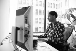 Black and white photo of woman sitting in chair looking at desktop computer.